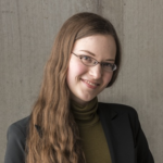 Woman in her thirties with long brown hair and glasses, wearing a blazer.